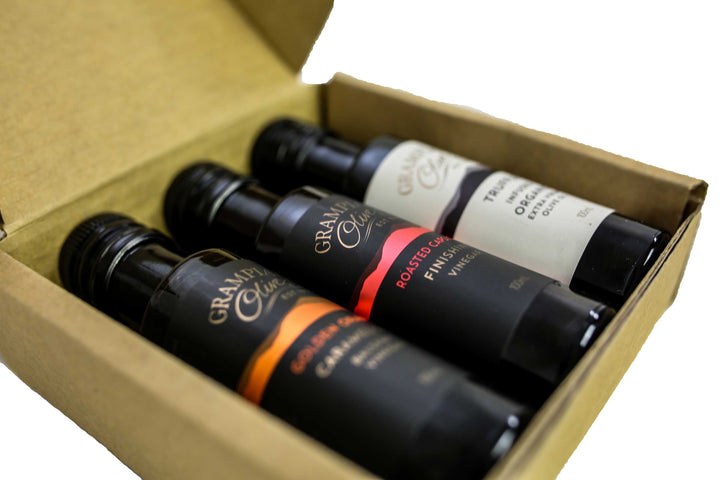 Three 100ml bottles of Grampians Olive Co. olive oil and balsamic with a cardboard box on a white background