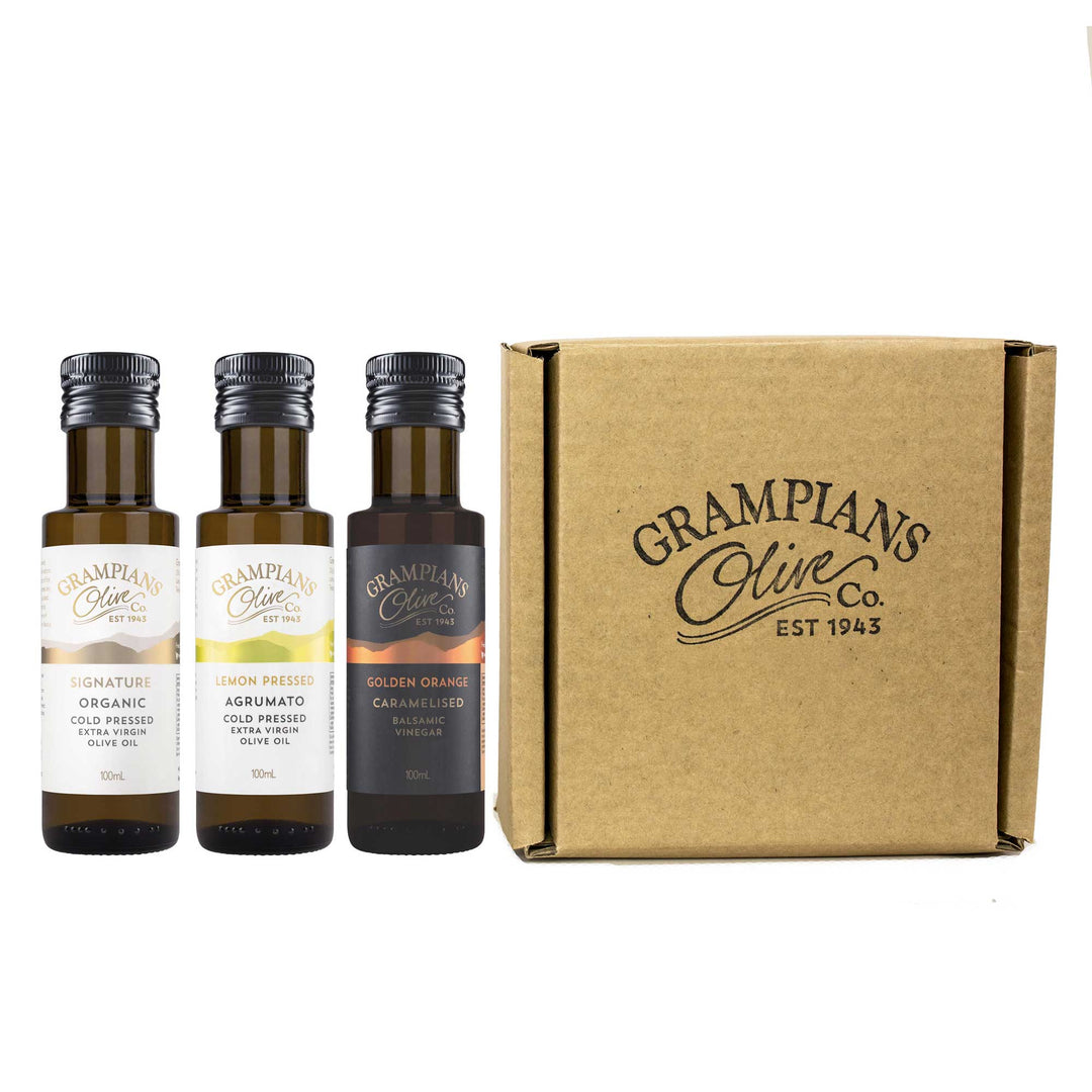 Three 100ml bottles of Grampians Olive Co. olive oil and balsamic with a cardboard box on a white background